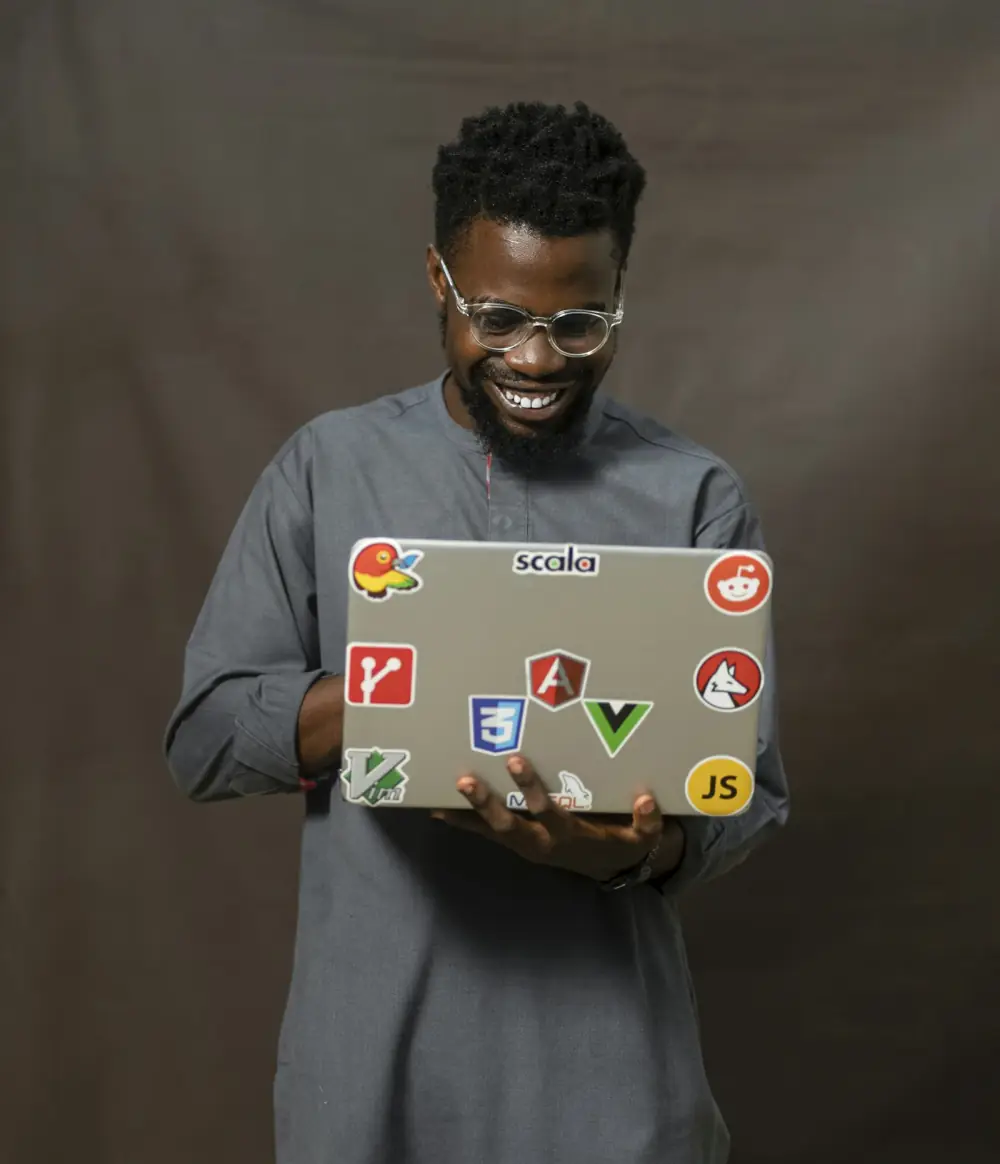 A smiling founder holds a laptop covered in developer stickers