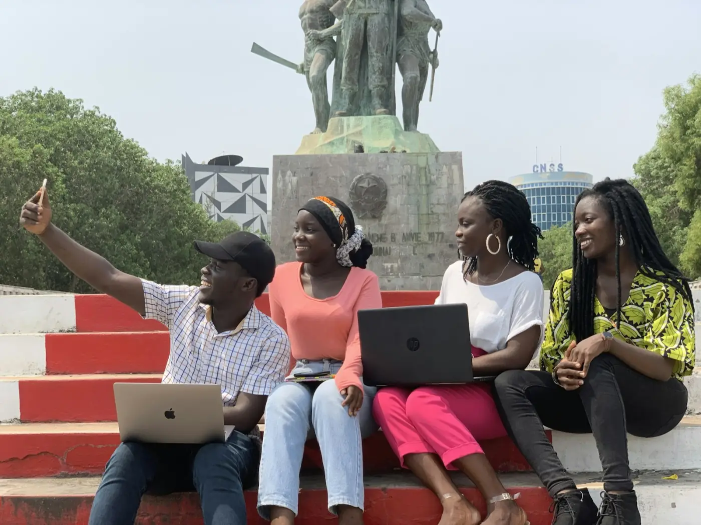Young founders with laptops sit together on red steps, taking a selfie